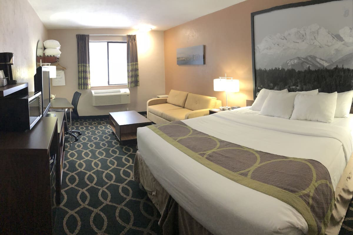 Ein Hotelzimmer mit einem großen Bett, einem Schreibtisch, einem Sessel, einer Couch, einer Schreibtischlampe und einem Bild an der Wand.