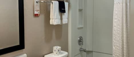 Une salle de bain équipée d’un WC, d’un lavabo et d’une douche. On y trouve des serviettes et un rouleau de papier toilette.