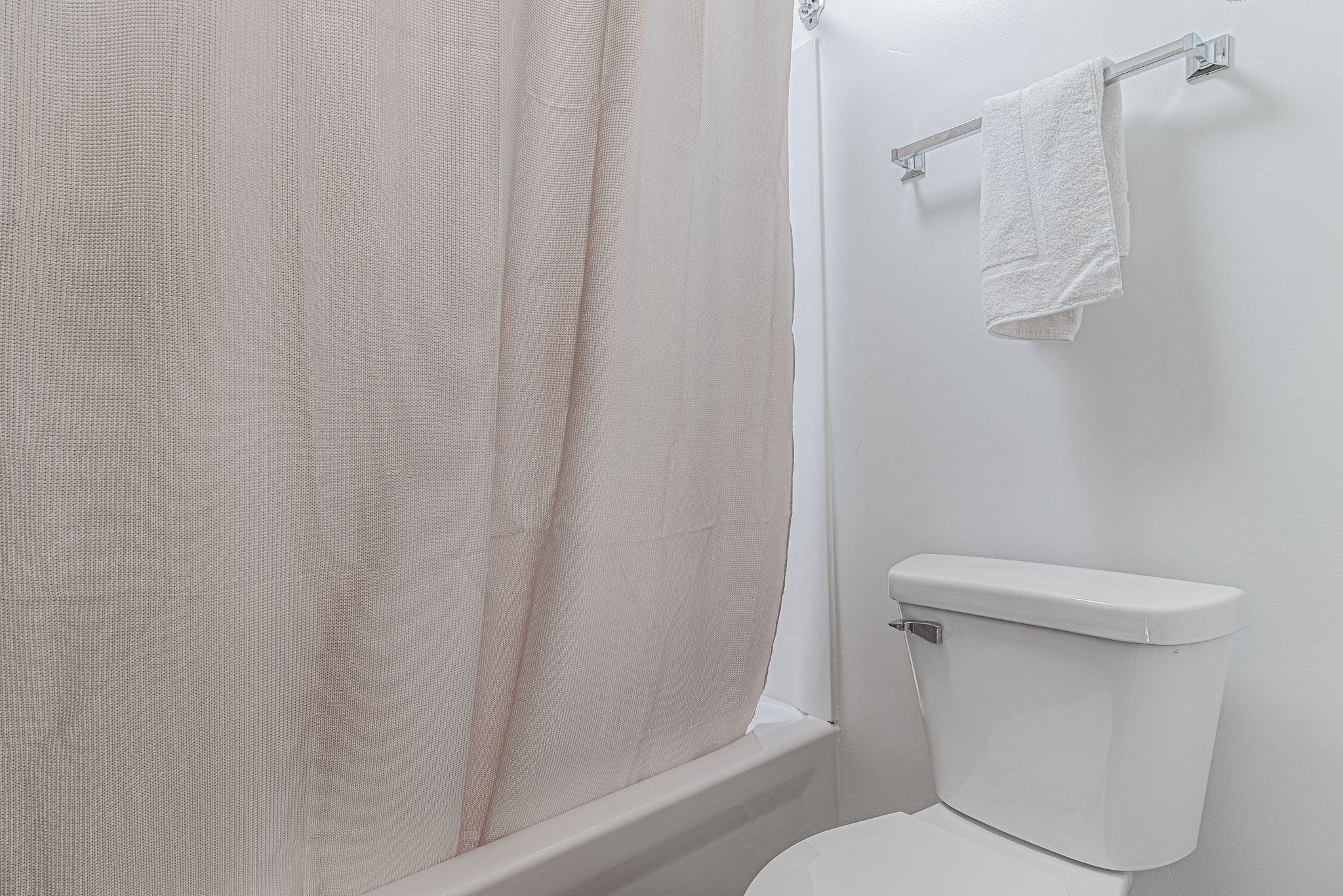 A bathroom with a shower curtain, a toilet, and a towel rack.
