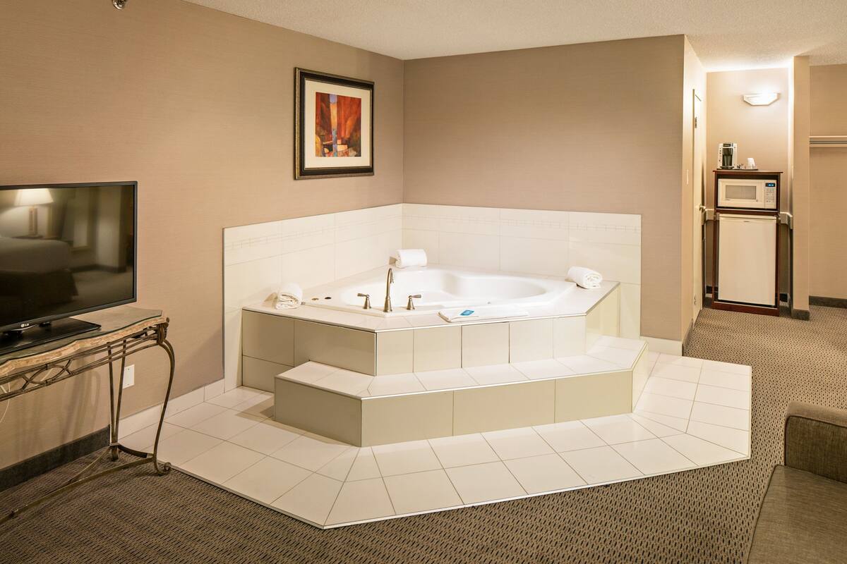 A modern bathroom with a large bathtub, a television, and a microwave.
