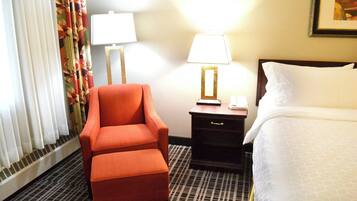 A hotel room with a single bed, a nightstand with a lamp, a chair, and a window with curtains.