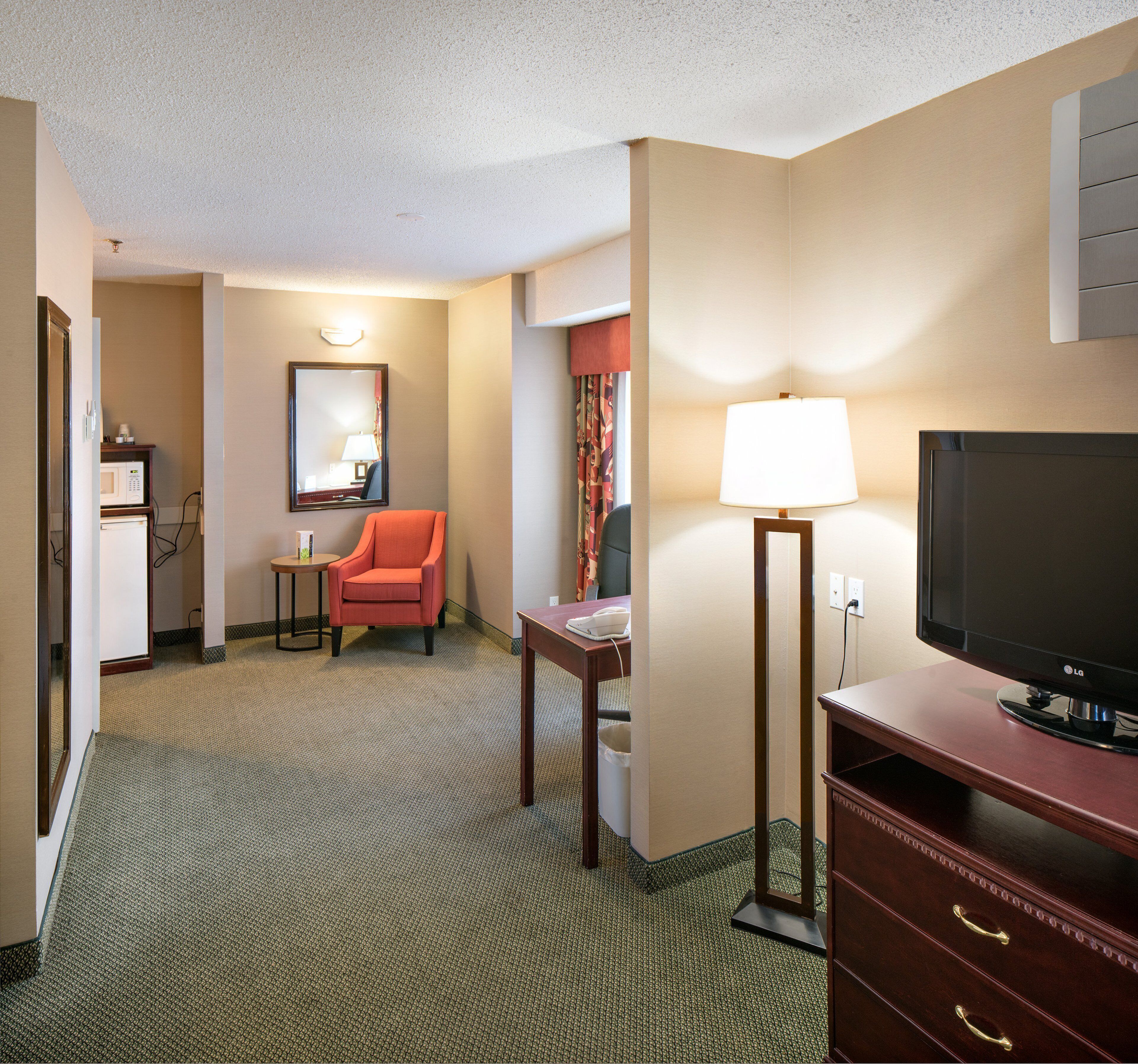 A hotel room with a television, a desk, a chair, a lamp, and a mirror.