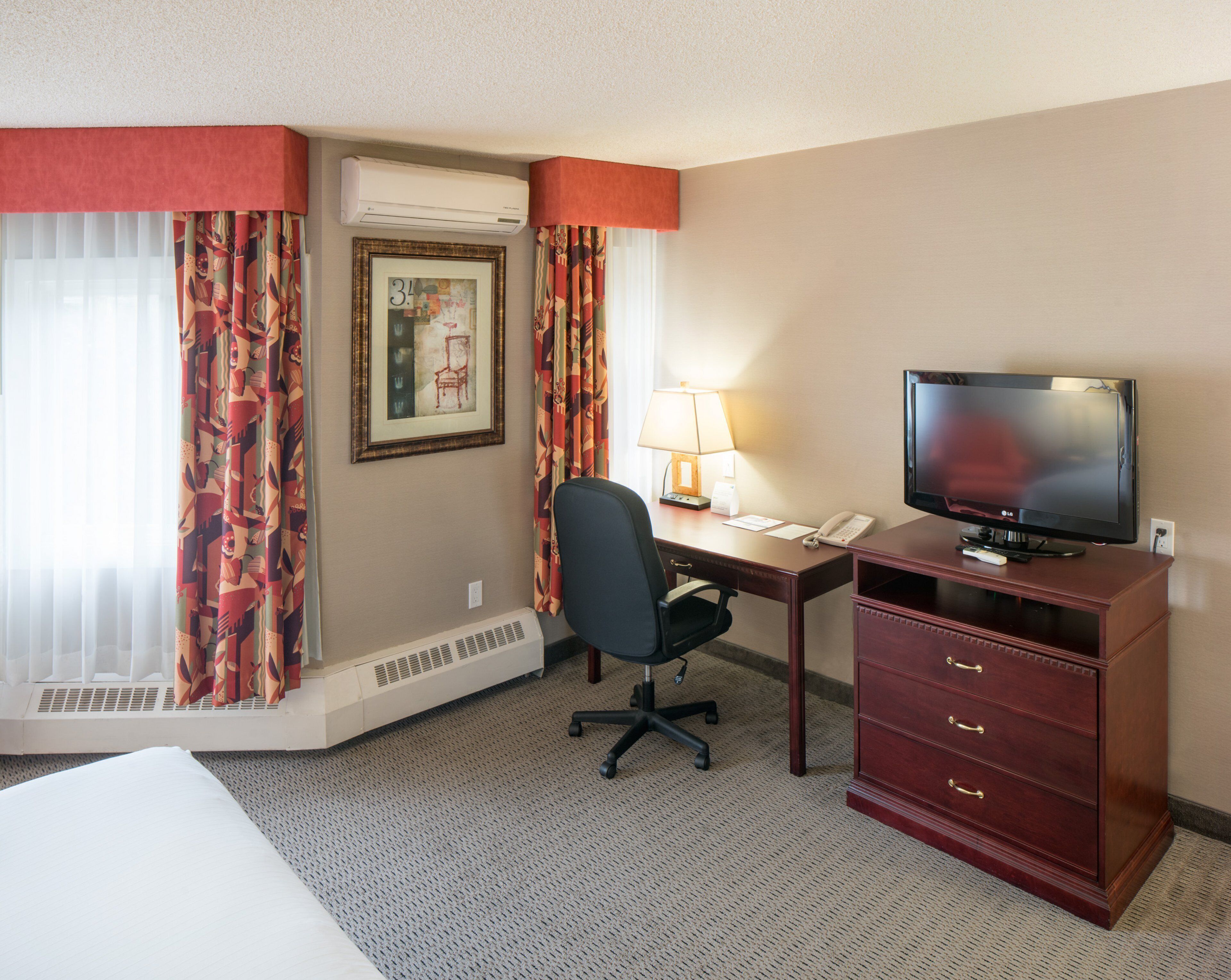 Habitación de hotel con cama, escritorio con silla, televisor, lámpara y teléfono.