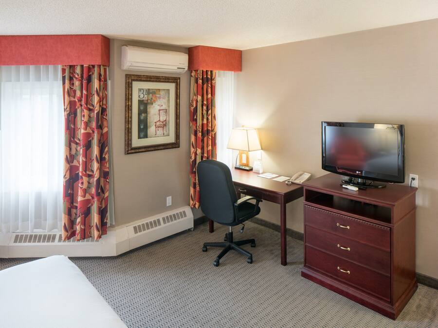 Une chambre d’hôtel comprenant un lit, un bureau avec une chaise, une télévision, une lampe et un téléphone.