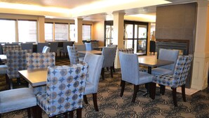 A dining area with patterned chairs and tables, a fireplace, and large windows.