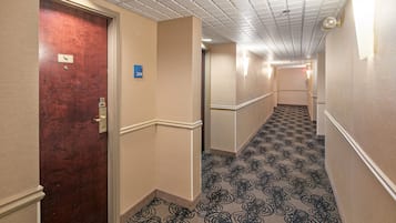 A hotel hallway with a patterned carpet, a wooden door, and a blue room number sign.