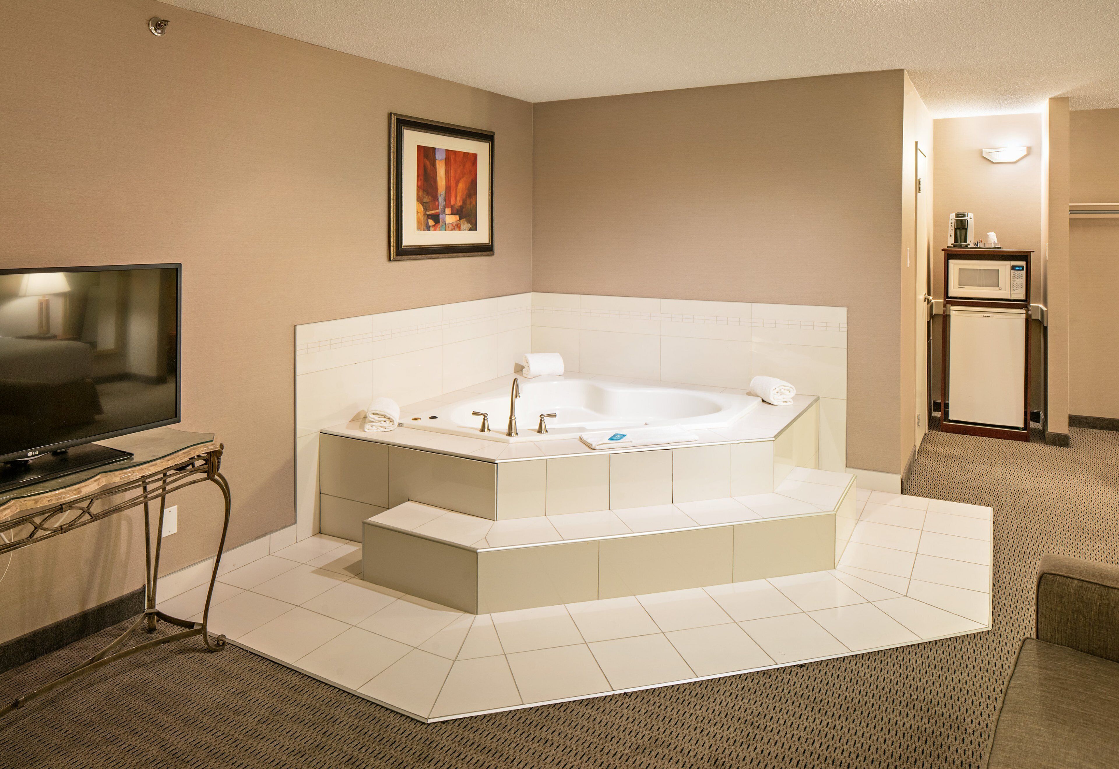 A modern bathroom with a large bathtub, a television, and a microwave.