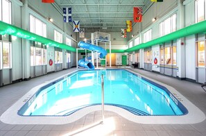 An indoor swimming pool with a blue slide, surrounded by windows and flags. - Holiday Inn Hinton by IHG (Hinton)