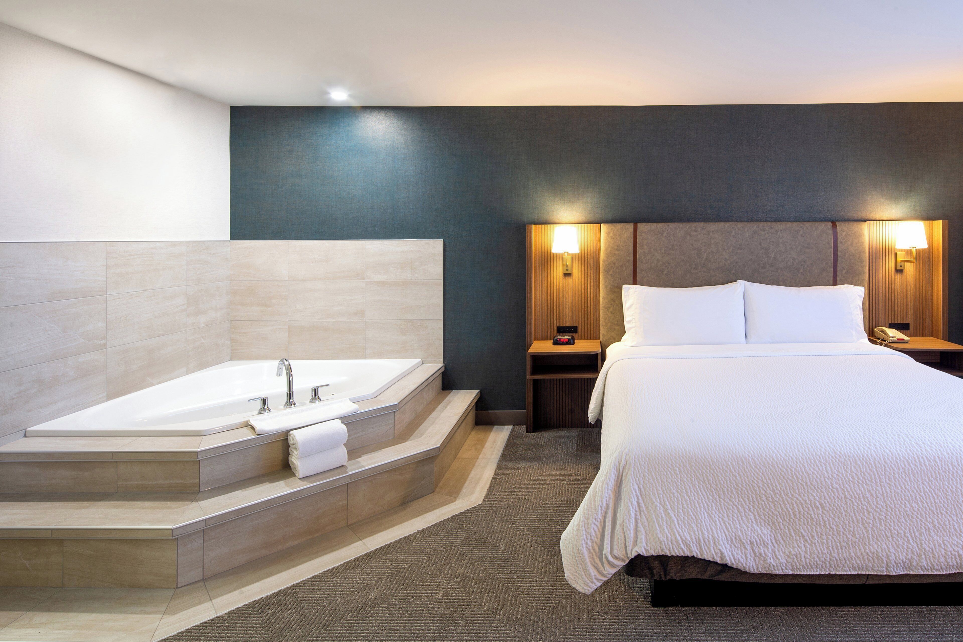 A hotel room with a large bed, a separate bathtub, and a bedside table with a lamp.