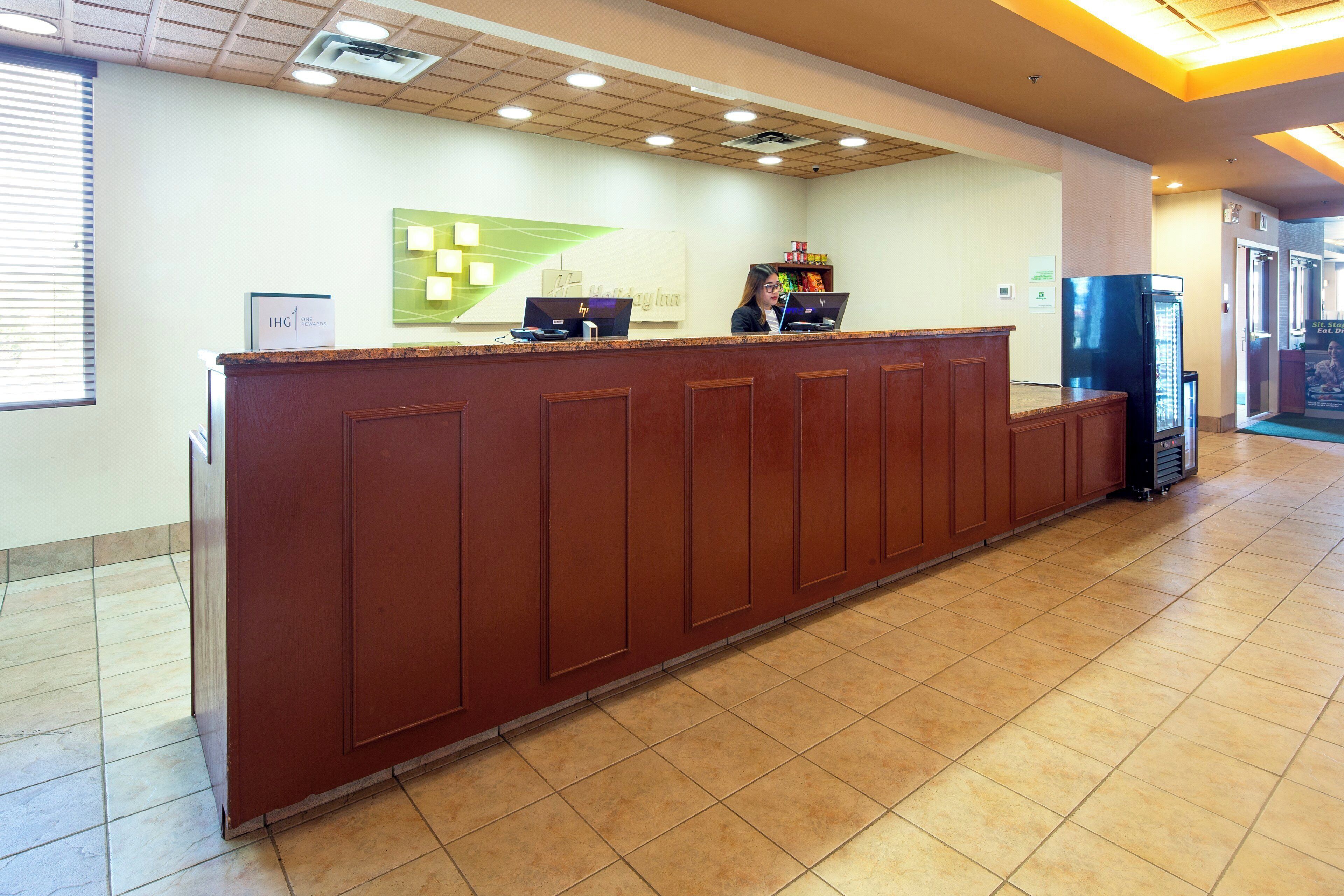 A reception desk with a brown counter, a green wall with a geometric design, and a tiled floor.