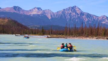 A group of people rafting on a river with mountains in the background.