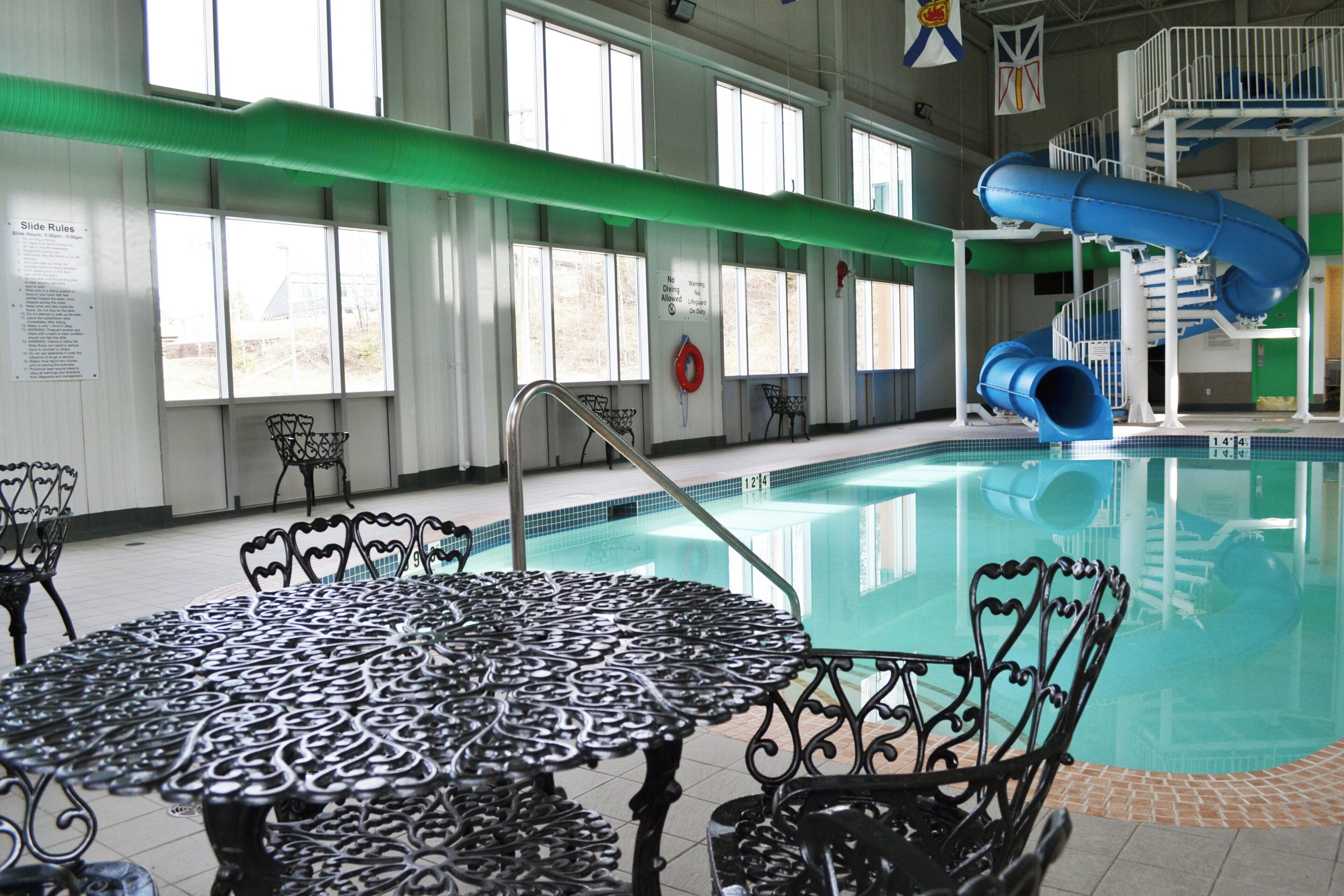 Una piscina interior con tobogán, un puesto de socorrista y una mesa con sillas.