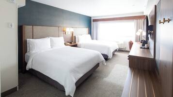 A hotel room with two beds, a desk, a TV, and a window with curtains.