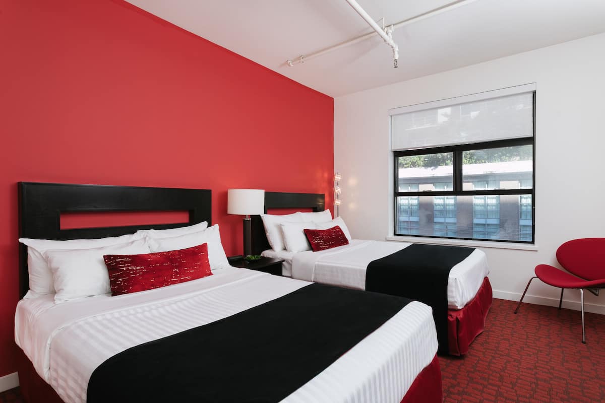 A hotel room with two beds, red walls, a large window, and a red chair.