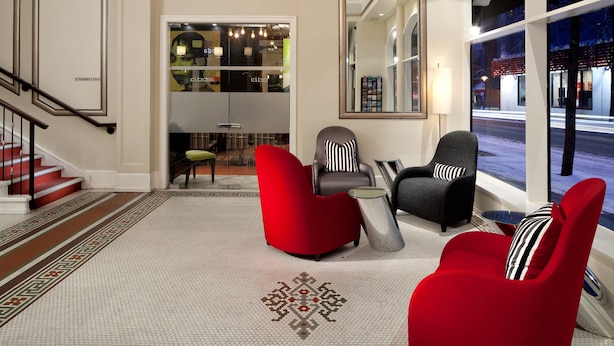 A lobby with a staircase, red chairs, a grey armchair, and a patterned floor. - Moda Hotel (Vancouver)