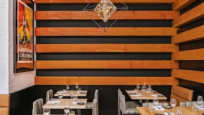 A restaurant interior with wooden panel walls, striped cushioned booths, and a geometric chandelier. - Moda Hotel (Vancouver)