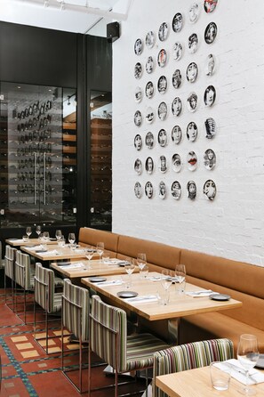 En restaurang med randiga, vadderade sittplatser, trÀbord och en vÀgg full med dekorativa tallrikar.