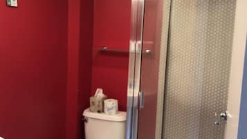 A bathroom with a toilet, a glass shower enclosure, and a towel rack with folded towels.