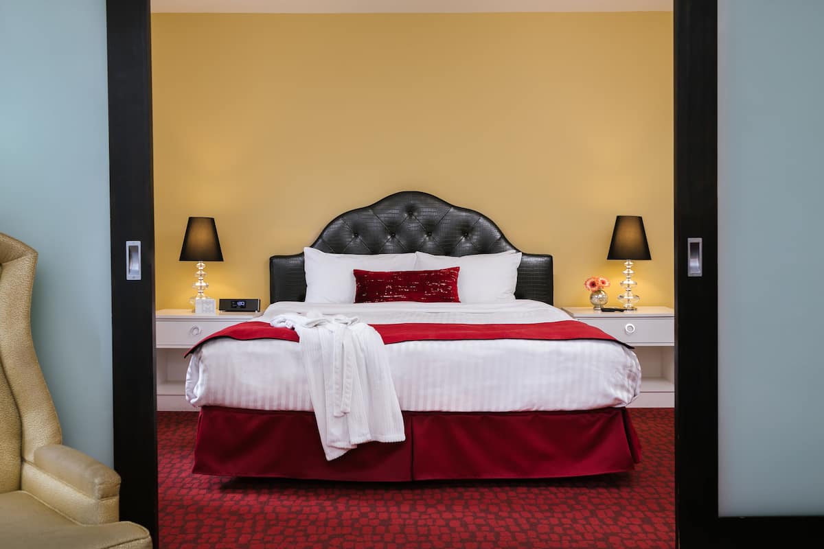 A hotel room with a large bed, two bedside tables, a chair, and a red carpet.