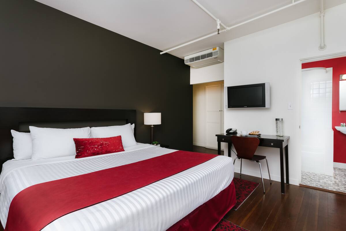 A hotel room with a large bed, a desk, a television, and a red accent wall.