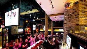 A bar with a brick wall, hanging lights, and a TV screen displaying sports. - Moda Hotel (Vancouver)