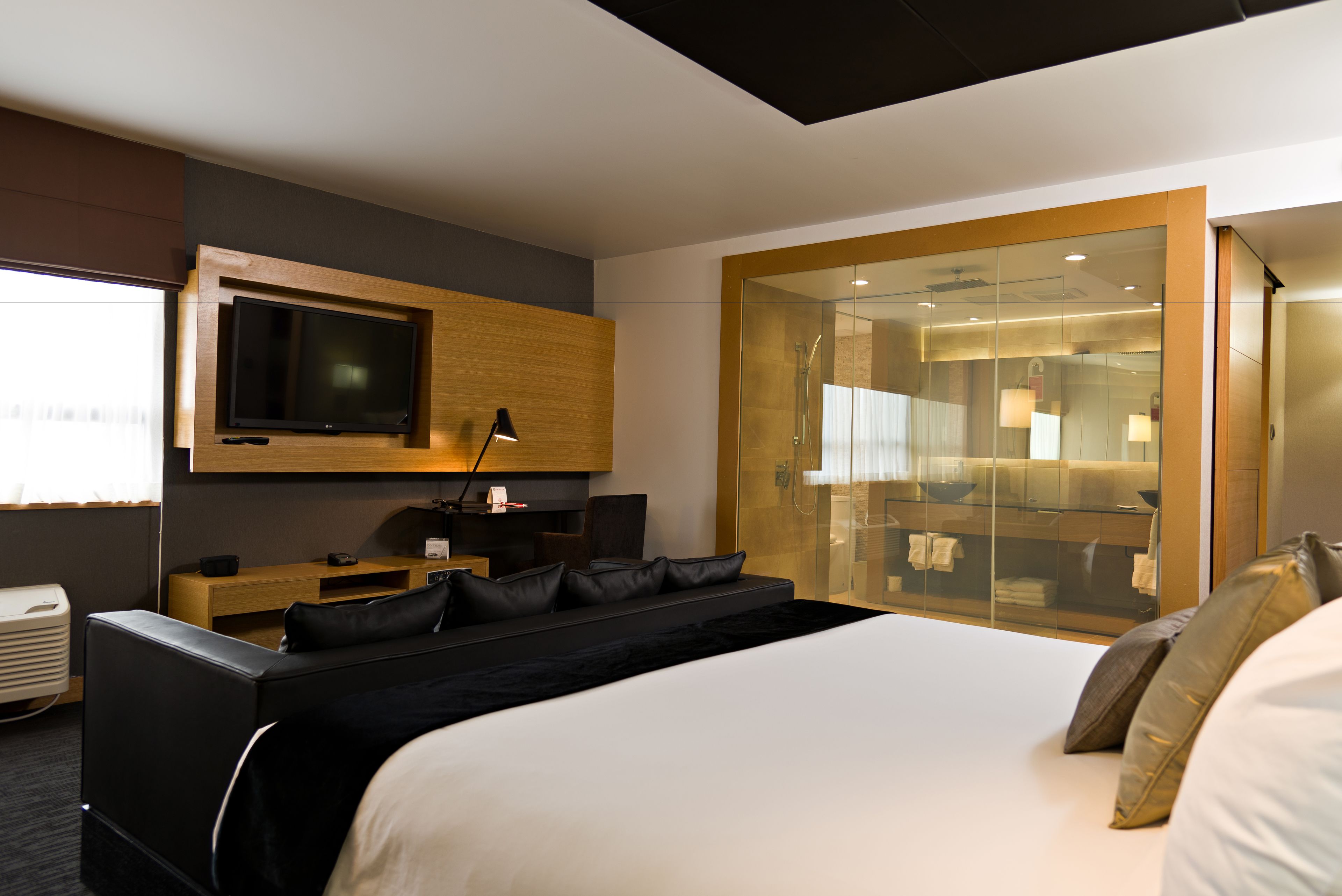 Ein modernes Hotelzimmer mit einem großen Bett, einem an der Wand befestigten Fernseher, einem Schreibtisch mit Stuhl und einem begehbaren Kleiderschrank mit Glastüren.
