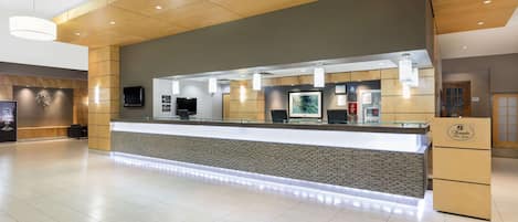 A modern reception area with a wooden ceiling, a reception desk, a flat-screen TV, and a digital display.