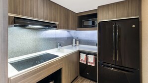 Μια μικρή, λειτουργική κουζίνα με εντοιχισμένο φούρνο μικροκυμάτων, ψυγείο από ανοξείδωτο ατσάλι και διπλό νεροχύτη.