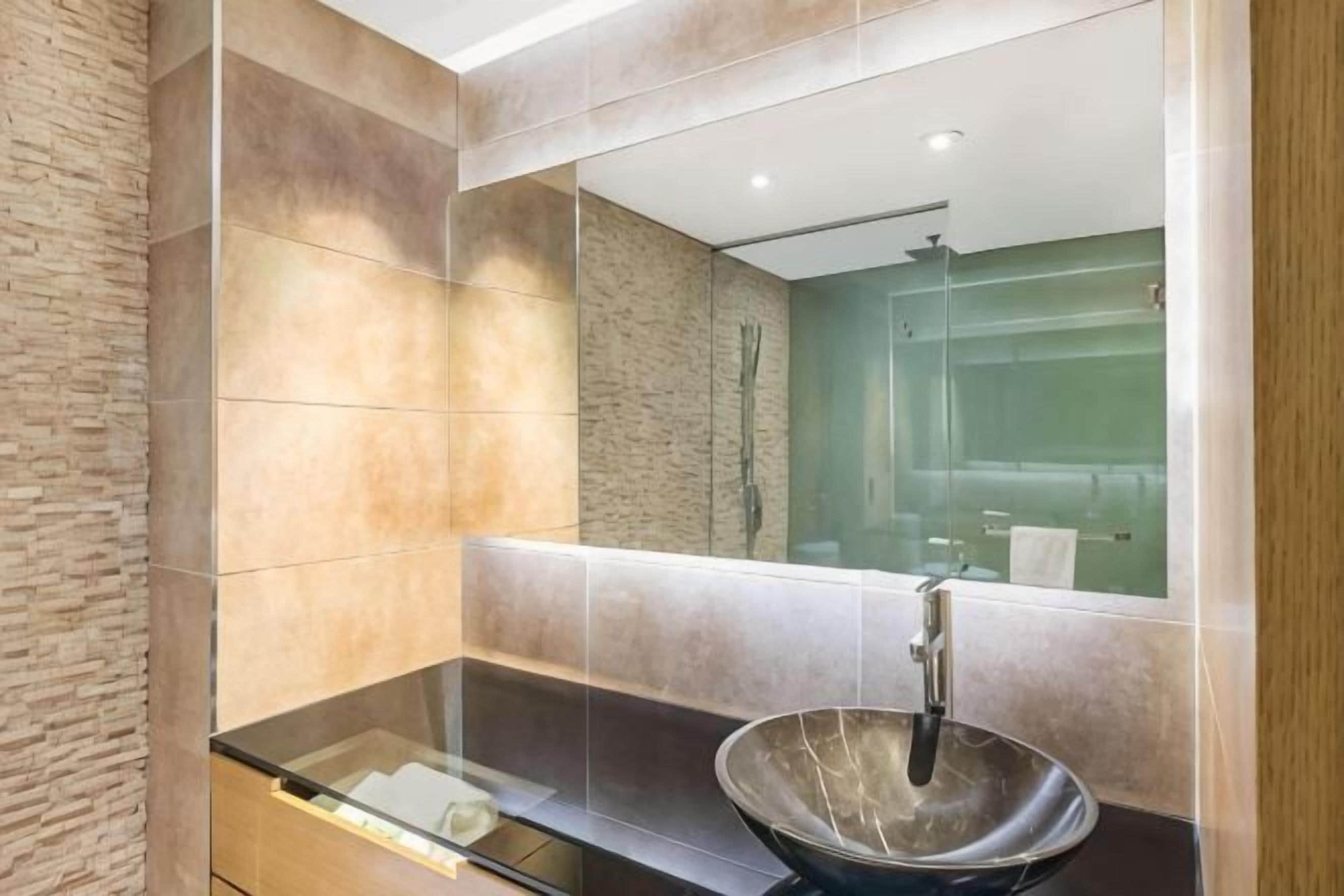 Un baño moderno con un espejo grande, un lavabo sobre encimera y una ducha con cerramiento de vidrio.