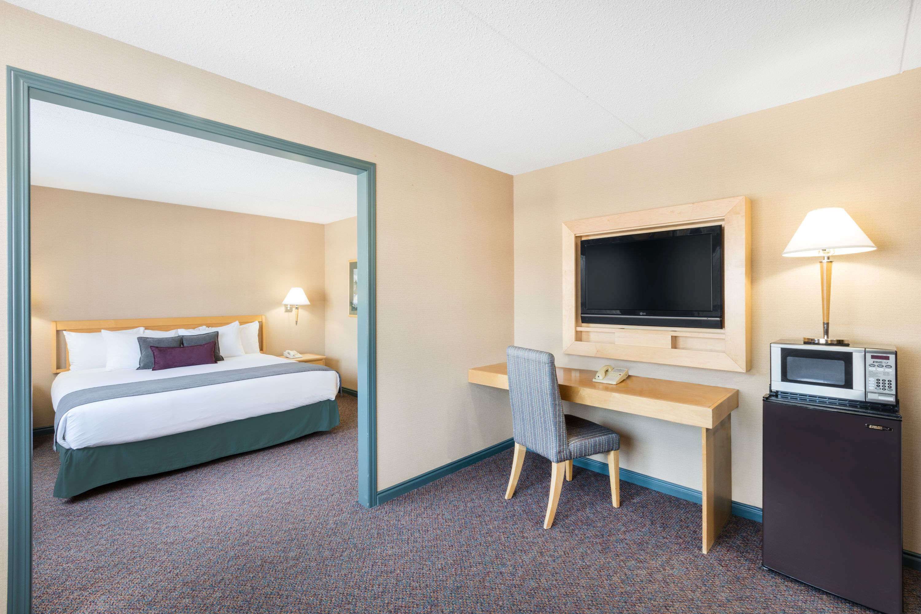 A hotel room with a bed, desk, chair, television, and a refrigerator.