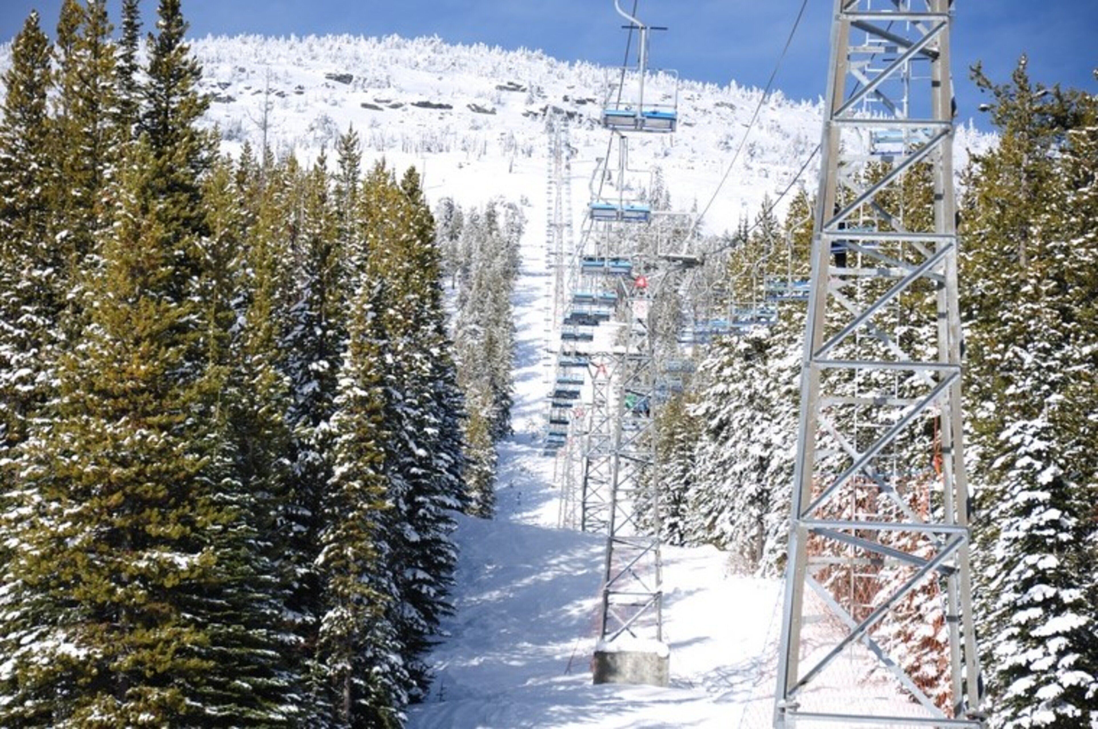 Pista de esqui coberta de neve, com um teleférico e árvores.