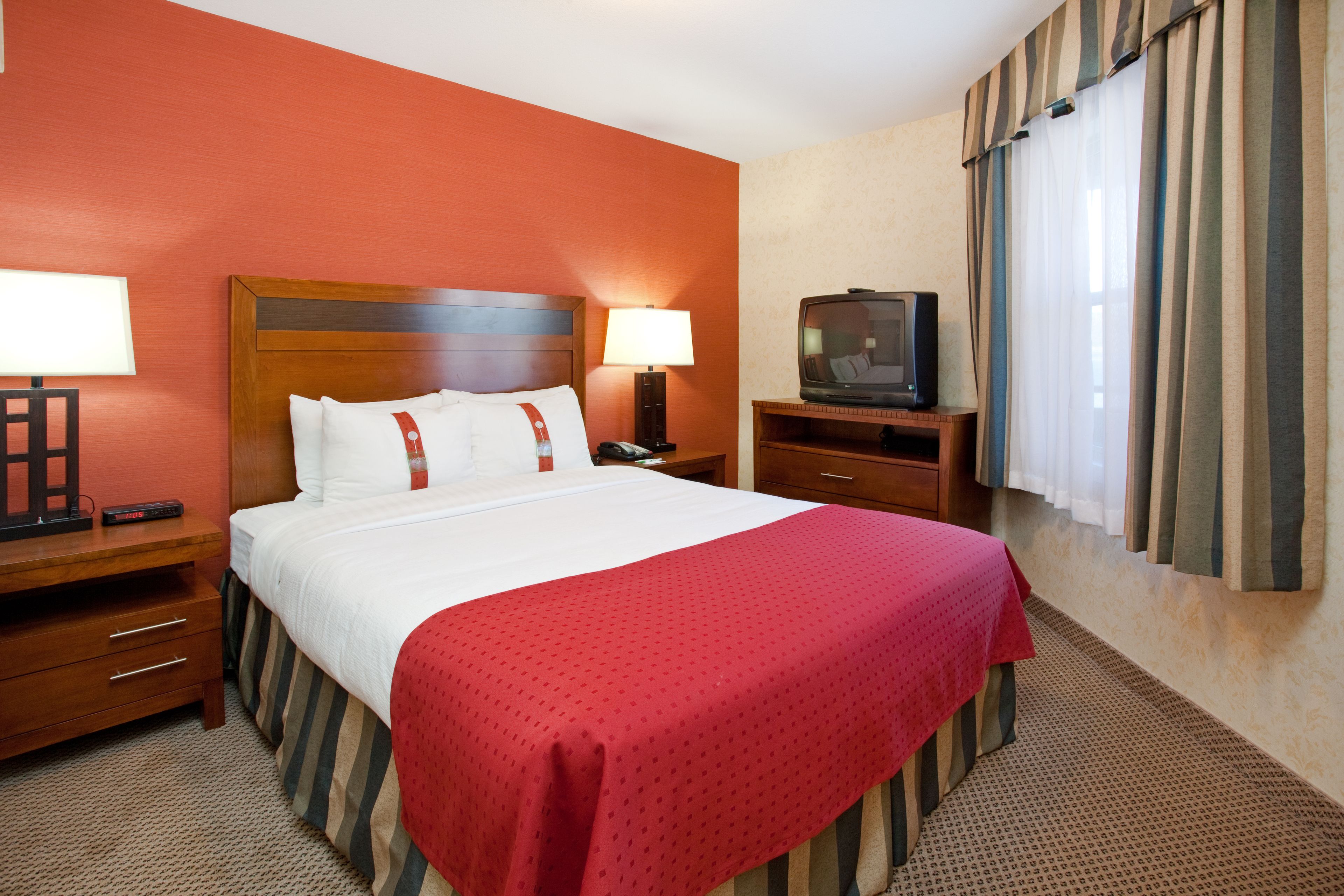 A hotel room with a large bed, two bedside tables, a TV, and a window with curtains.