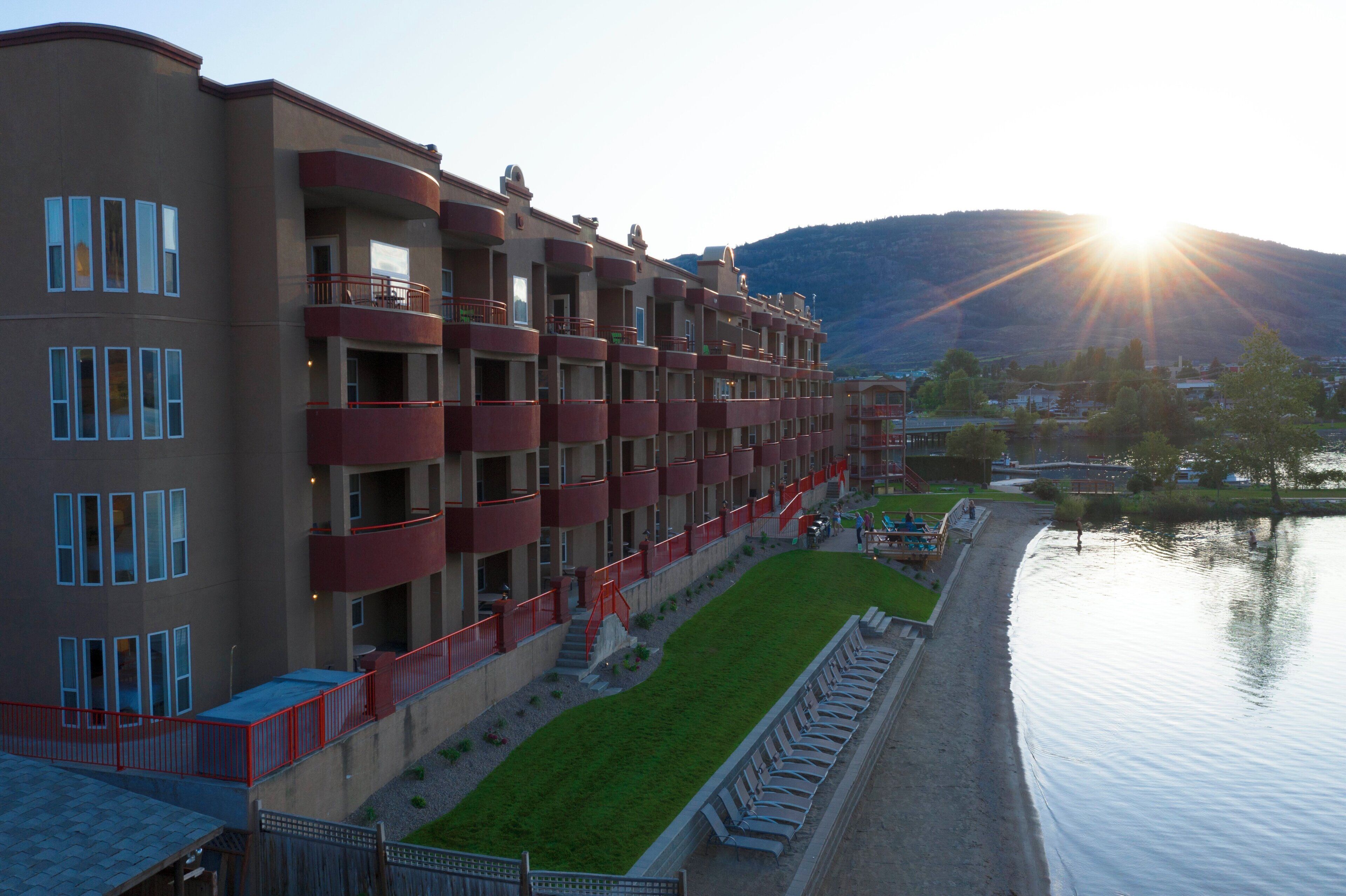 A multi-story hotel with balconies, a grassy area, and a body of water.