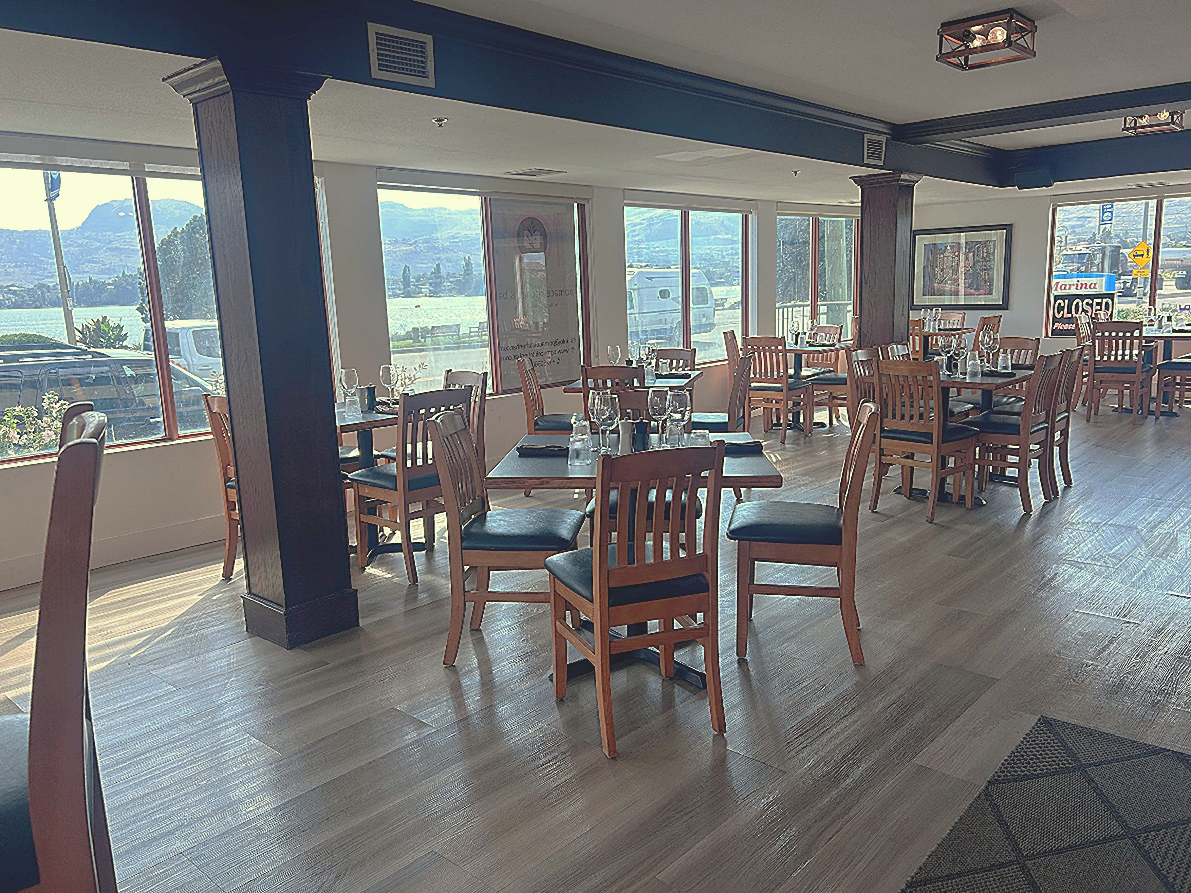 A restaurant with wooden tables and chairs, large windows with a view, and a high ceiling.