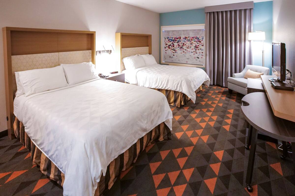 Habitación de hotel con dos camas, un escritorio, una silla y un televisor.