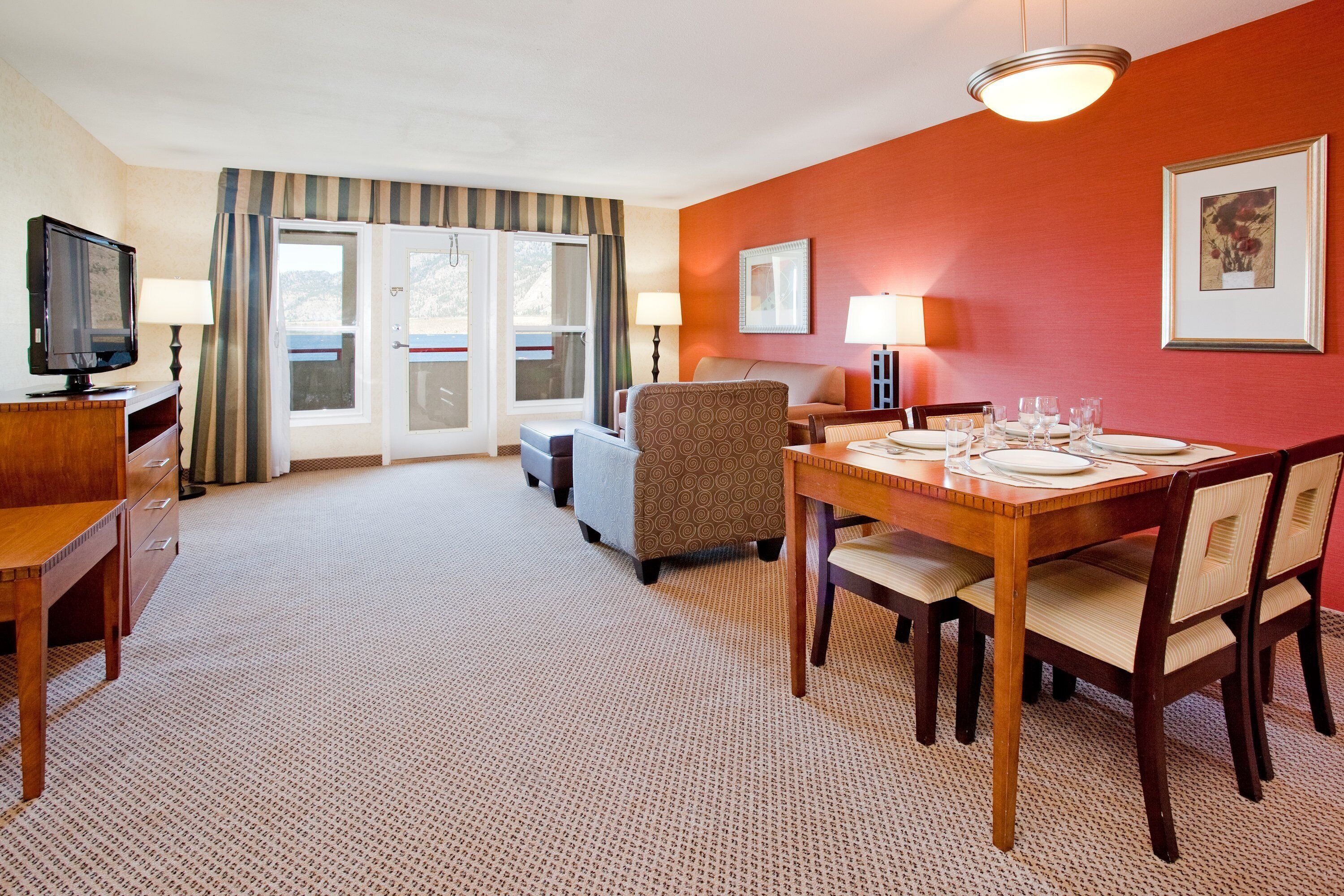 A hotel room with a dining area, a television, and a window with curtains.