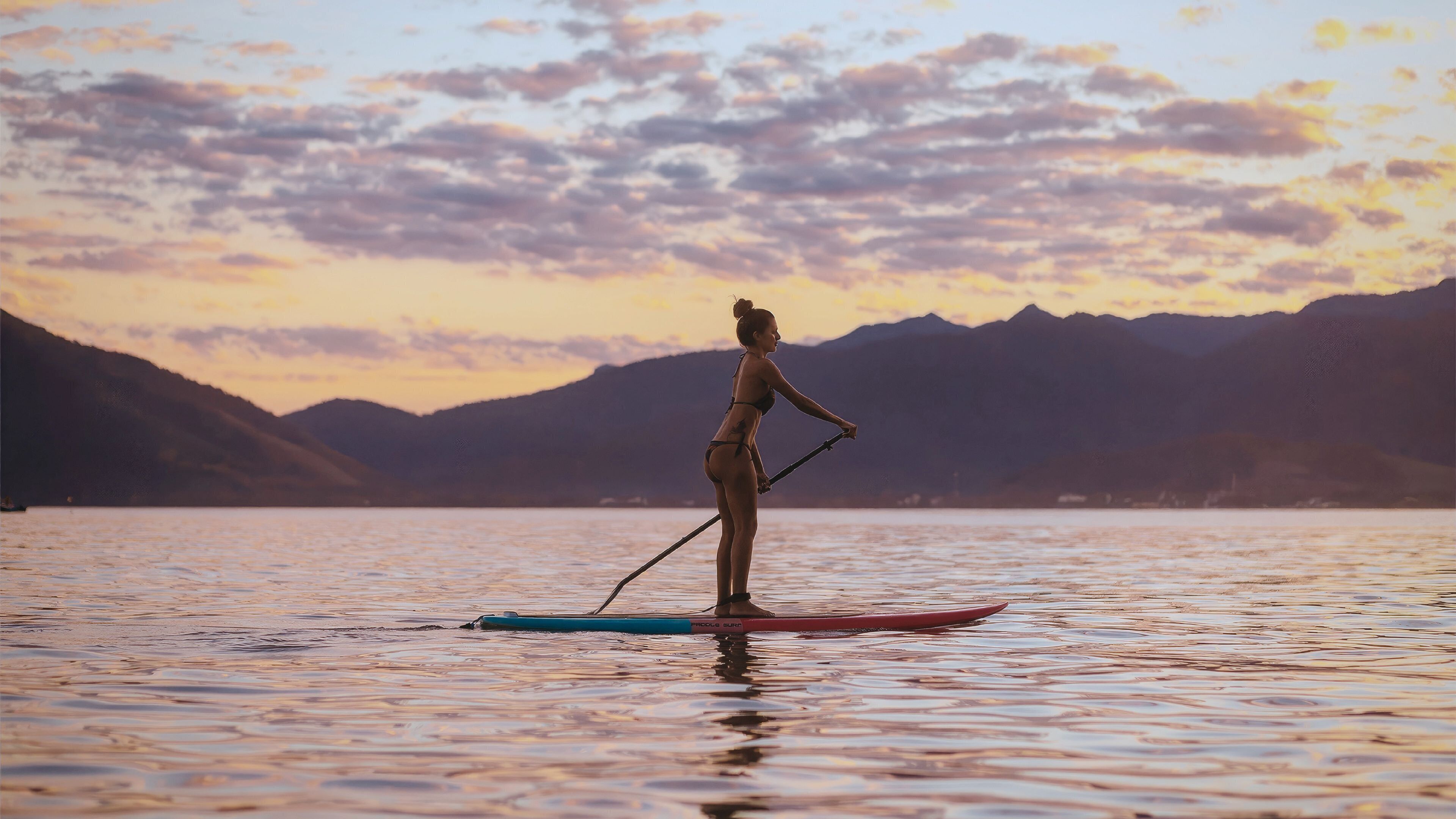 A person paddleboarding on a calm lake with mountains in the background.