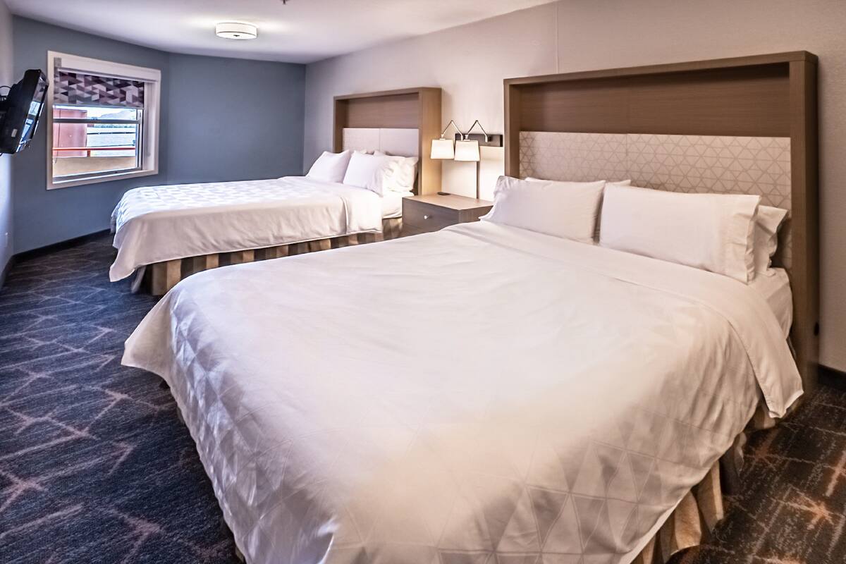 Habitación de hotel con dos camas, una mesita de noche con lámparas, televisión y ventana con vistas.