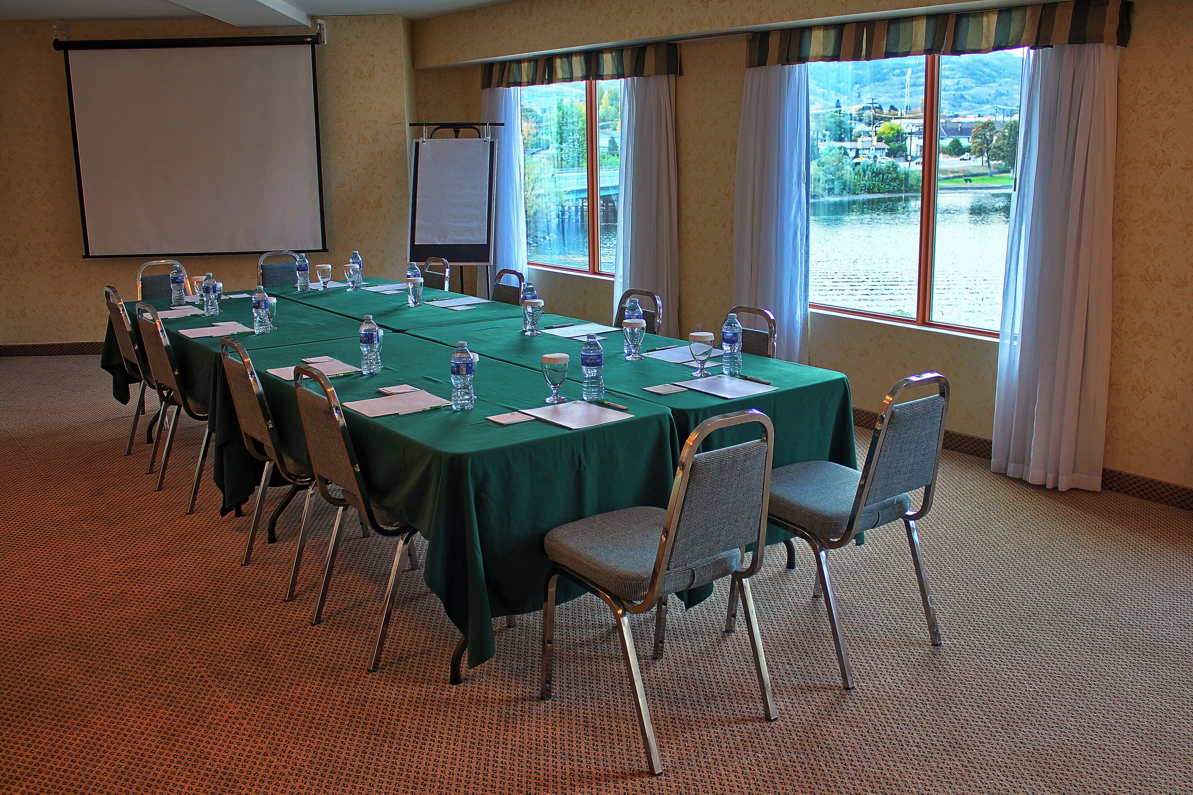 A conference room with a long table, chairs, water bottles, and a projector screen.