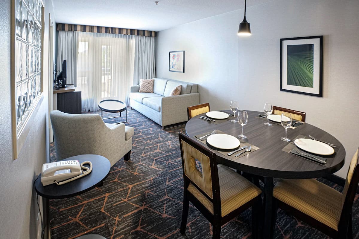 Habitación de hotel con comedor, sofá, una pequeña mesa con teléfono y piso alfombrado.