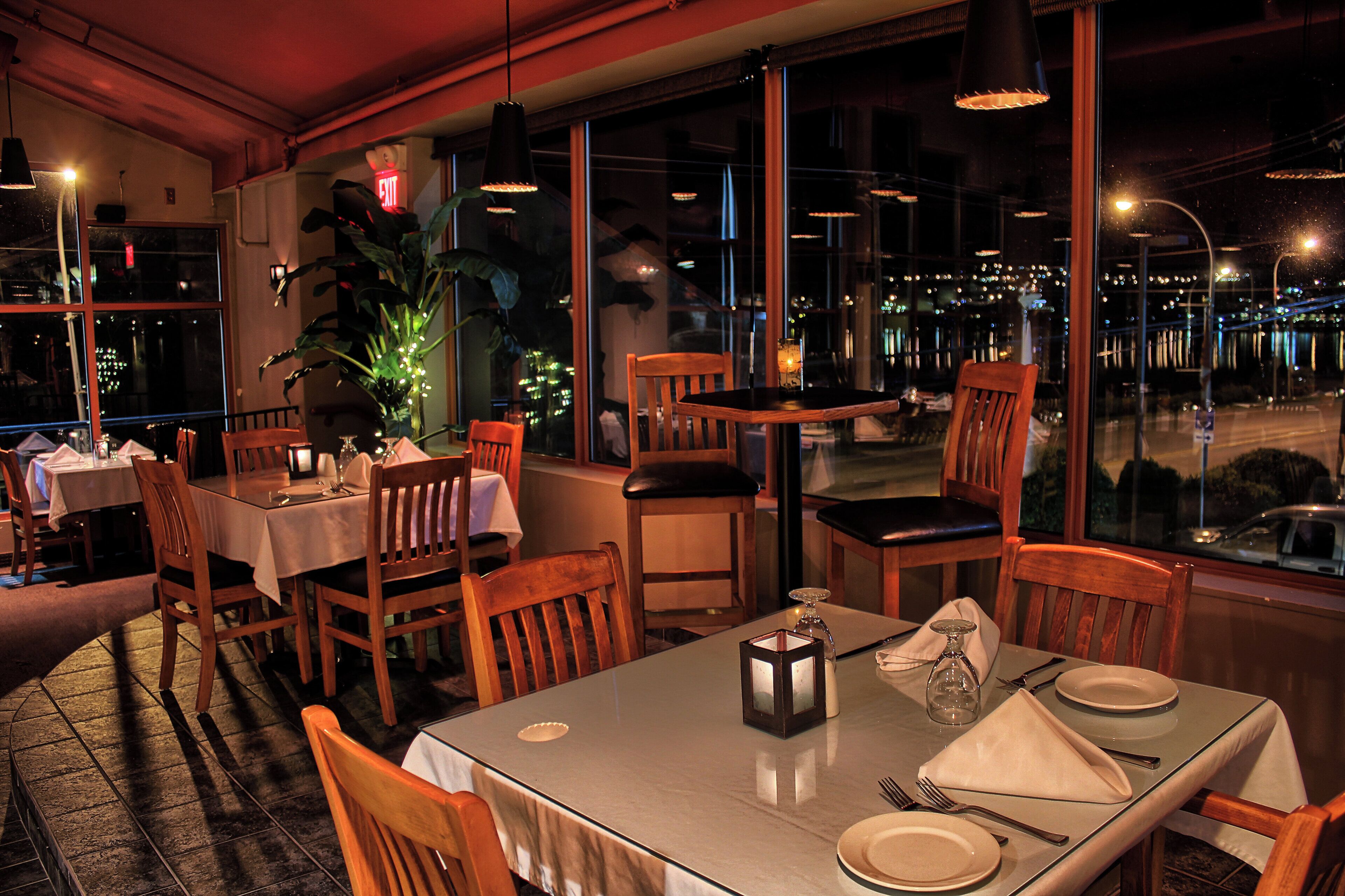 A restaurant with tables set for dining, chairs, and a large window with a city view.