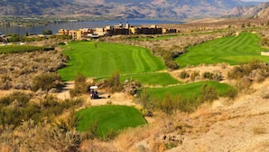 A golf course with a clubhouse, a lake, and mountains in the background.