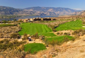 Un parcours de golf doté d’un club-house, d’un lac et avec des montagnes en toile de fond.
