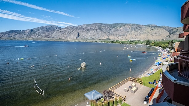 A lakeside view with boats, swimmers, and a mountainous backdrop.