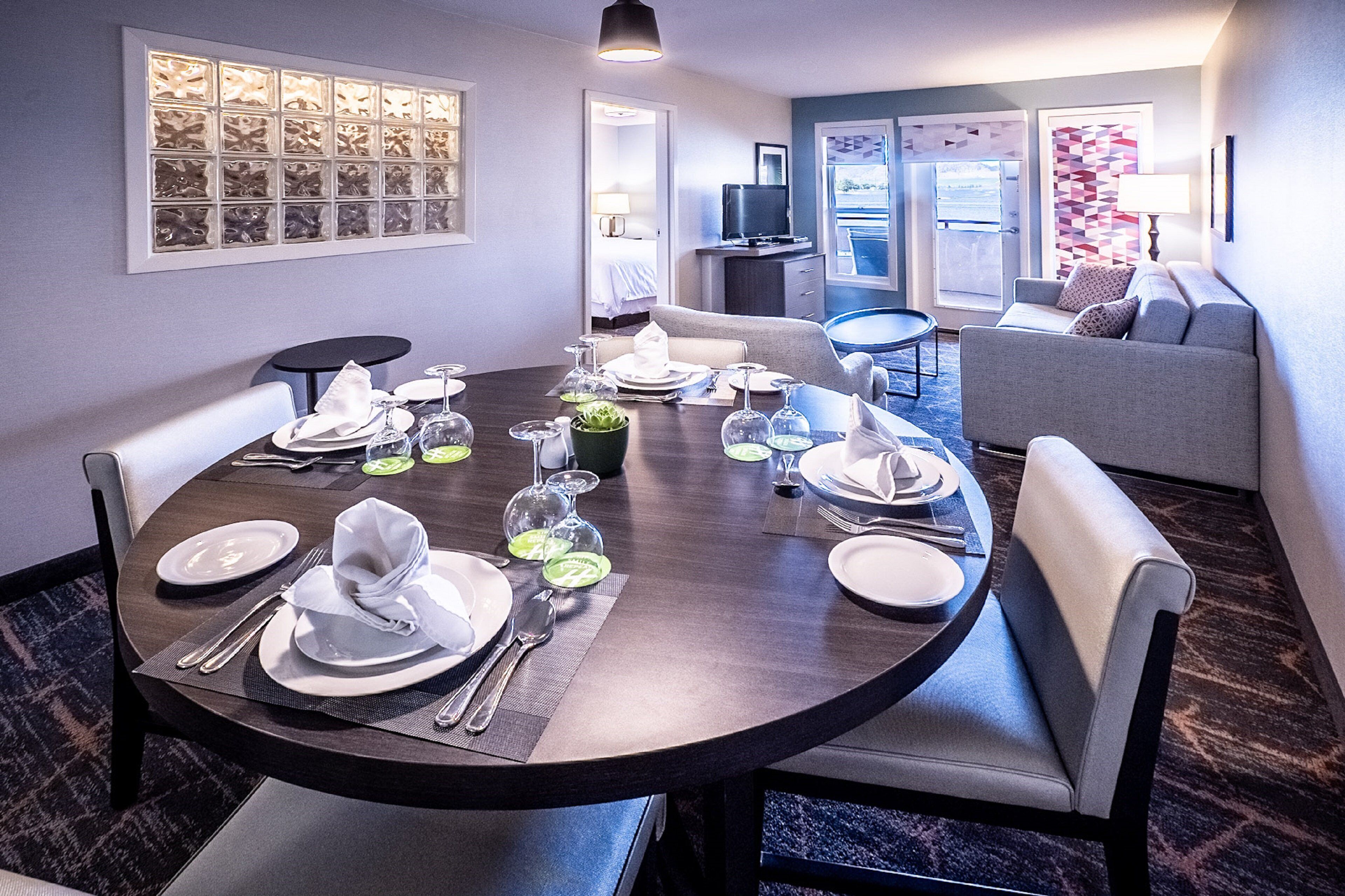A dining area with a round table set for six, a sofa, and a television in the background.