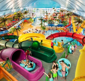 A water park with multiple slides and pools, indoor seating areas, and a covered section with a view of the cityscape.