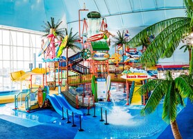 Parque acuático interior con toboganes, piscina de olas y un letrero que dice 'Beach House'.