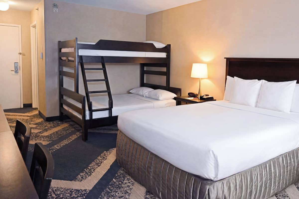 Ein Hotelzimmer mit einem Etagenbett, einem Einzelbett, einem Schreibtisch mit Lampe und einem gemusterten Teppich.