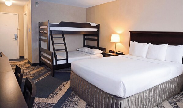 Une chambre d’hôtel avec un lit superposé, un lit simple, un bureau avec une lampe et un tapis à motifs.