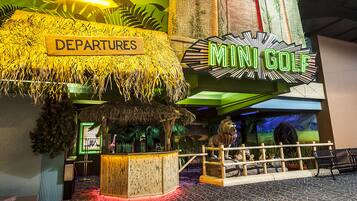 A mini-golf area with a sign labeled "Departures" and a neon sign for "Mini Golf".
